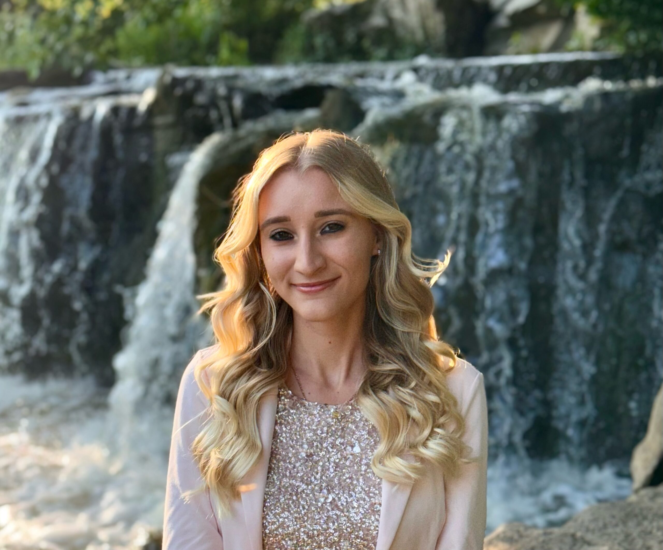 Nicole Zalewski, counseling intern and Certified Life Coach with expertise in positive psychology, art life coaching, and child autism spectrum interventions, smiling in front of a serene waterfall.