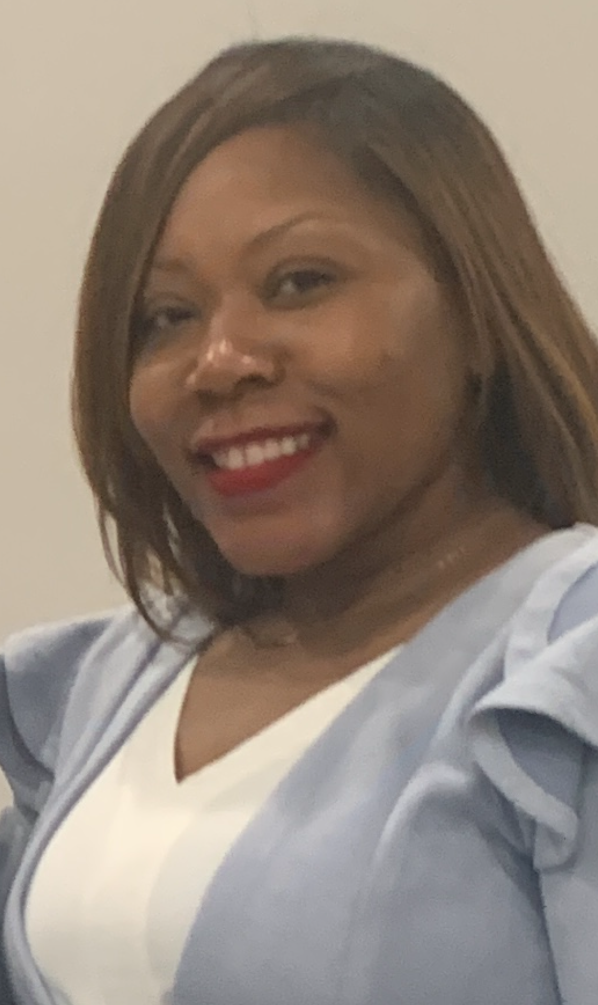 Kenya Spann smiling in a light blue blazer and white top, posing in front of a neutral background.